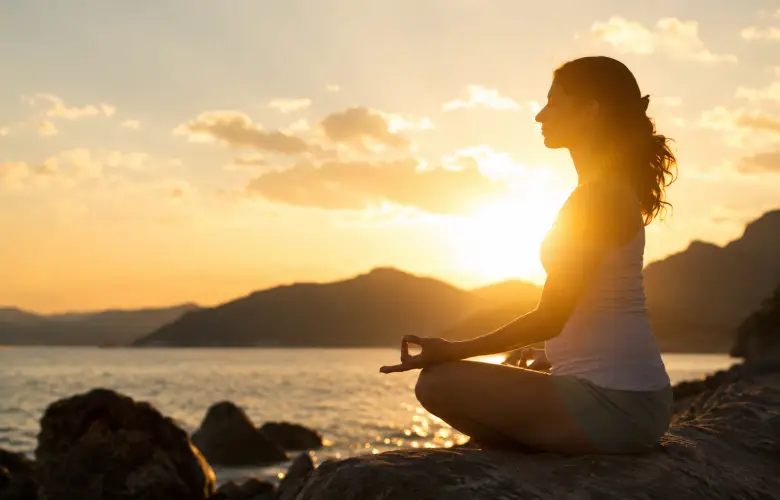 Mujer meditando sentada frente a un paisaje al atardecer