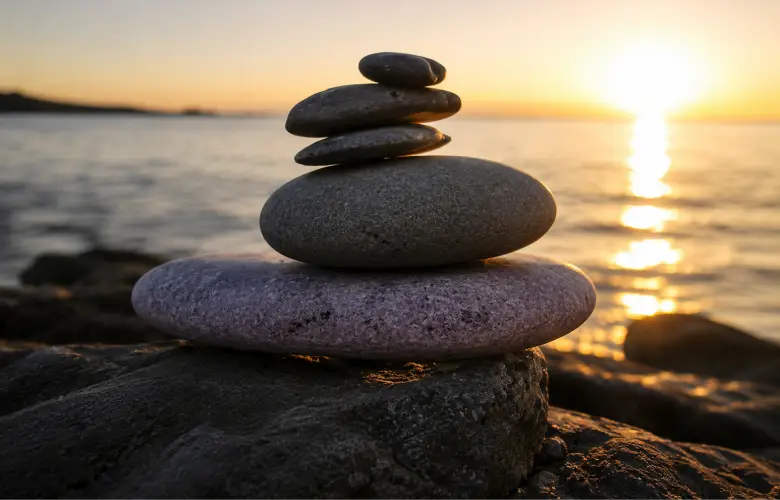 Piedras apiladas junto al mar al atardecer como símbolo de equilibrio y calma